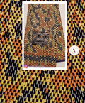 A folded fabric sample with a bold geometric ikat pattern in orange, yellow, black, and white, featuring a 'woodin' brand label. The fabric is presented in a white-bordered frame against a matching patterned background.