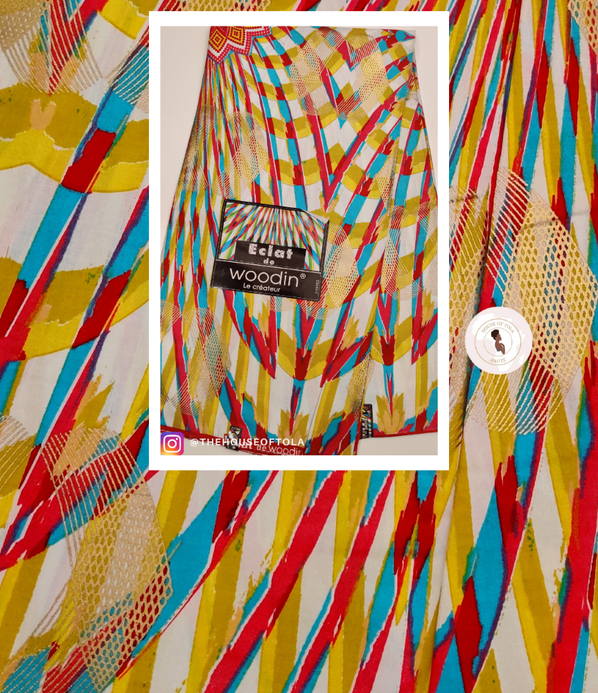 A folded patterned fabric item with a colorful geometric print is shown in a centered white-bordered inset over a matching fabric background. The print features bold diagonal stripes and abstract brushstroke shapes in red, yellow, blue, and white, with a visible Woodin label.